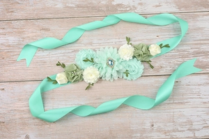 Close-up of mint green maternity sash with handcrafted floral cluster and blue teardrop gem
