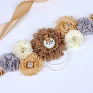 Close-up of floral maternity sash with Mommy To Be badge, bear toy and pearl chains
