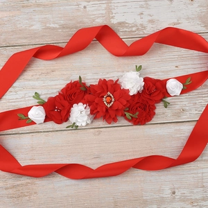 Detailed macro view of handmade red satin sash featuring fabric flowers and emerald green leaves