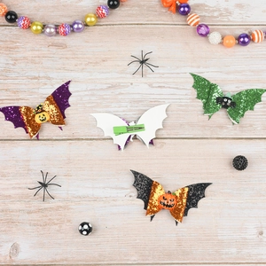 Macro detail of glittery Halloween bat wing hair clips with pumpkin and spider motifs