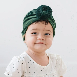 Detail of dark green velvet baby donut knot hat showing soft texture on an infant model
