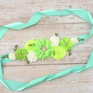 Detail of mint green floral maternity sash with faux pearls and rhinestones on wood