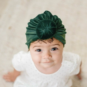Detailed close-up of dark green velvet baby turban hat with top knot on infant model