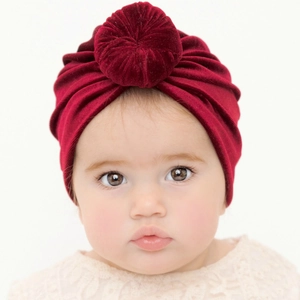 Infant velvet turban hat with donut knot in burgundy worn by a baby model