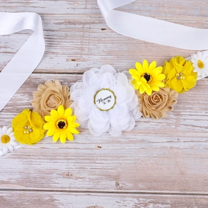 Detail of Mom To Be sash featuring handmade sunflower, beige rose, and white daisy floral cluster