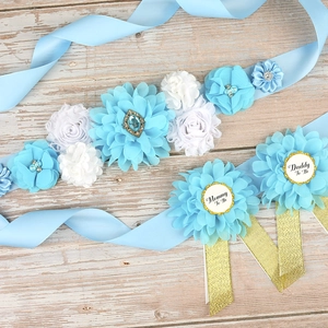 Detail of baby shower set with light blue flower sash and Mommy to Be badges on wood