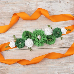 Detail of maternity sash with green silk flowers, rhinestone brooch, and orange ribbon