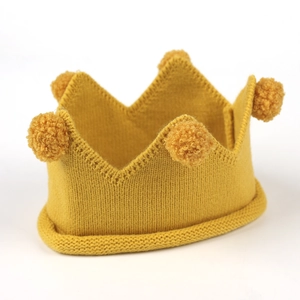 Détail du bonnet couronne tricoté jaune gingembre pour bébé avec pompons et texture