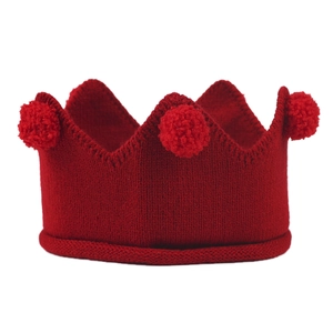 Détail d'un bonnet couronne en tricot rouge pour bébé avec pompons doux sur le dessus