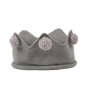 Détail d'un bandeau couronne en tricot gris pour bébé orné de trois pompons doux sur le haut