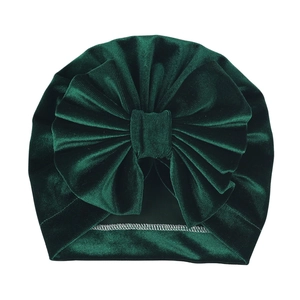 Detail of deep green velvet baby turban hat featuring a large decorative bow and soft texture