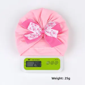 Bonnet turban bébé rose avec gros nœud et imprimé love sur balance pesant 25g