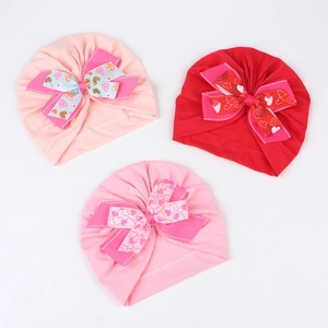 Détail de bonnets turban bébé roses et rouges avec grands nœuds à motifs cœurs