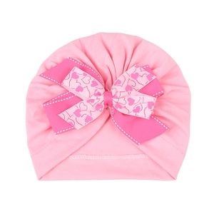 Détail du bonnet turban rose pour bébé avec un grand nœud et motif de cœurs