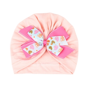 Détail d'un bonnet turban rose pour bébé avec un nœud double à motifs de petits cœurs