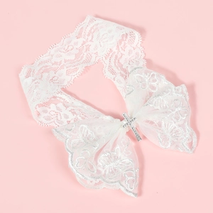 Détail du bandeau en dentelle blanche avec croix en strass et nœud sur fond rose tendre