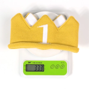 Detailed macro view showing a yellow knitted crown hat weighing 33.3 grams on a digital scale