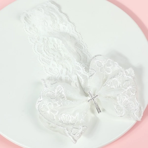 Détail d'un bandeau bébé en dentelle blanche avec nœud et croix en strass sur rose