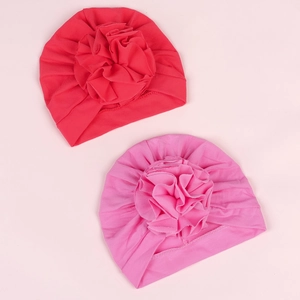 Detailed flat lay of red and pink baby turban hats with large layered 3D floral decorations