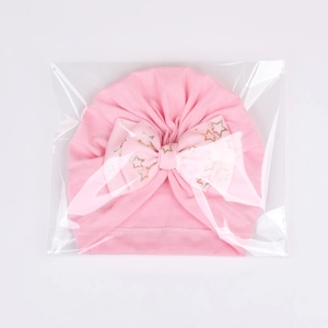 Detail view of pink baby turban hat with golden star bow in plastic packaging