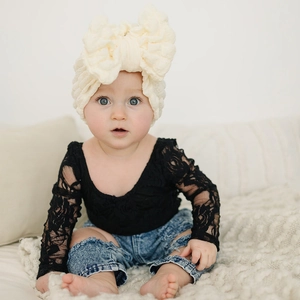 Detail of baby outfit featuring oversized bow headband and black lace top with jeans