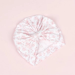 Détail d'un bonnet turban pour bébé avec motif floral rose et un grand nœud décoratif
