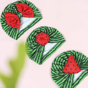 Three-piece infant watermelon style hats with bows and pom-poms on a soft pink background