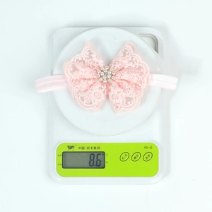 Bandeau en dentelle rose avec nœud et perles, pesant 8.6g sur une balance blanche