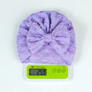 Detail view of a lavender baby turban hat with a bow on a scale weighing 25.9 grams
