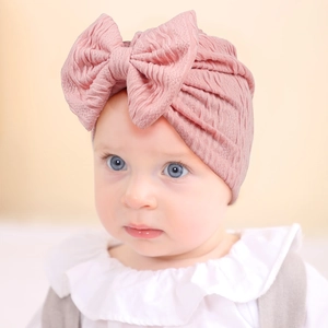 Detail of pink baby turban hat featuring a large bow and soft ribbed texture on infant