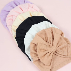 Detail of six colorful soft ribbed knit baby hats with large bows and pleated texture