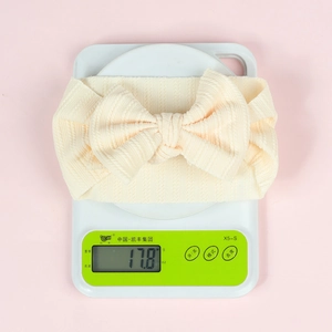 Detail shot of a creamy white elastic bow headband on a scale weighing 17.8g
