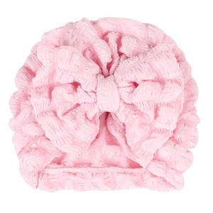 Pink waffle-knit baby turban hat with a large bow decoration on white background