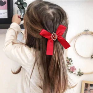 Detailansicht einer roten Satinschleife mit Strassstein im Haar eines kleinen Mädchens