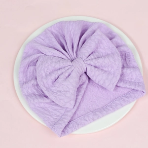 Detailed flat lay of lavender knitted baby turban with large textured bow on a white plate