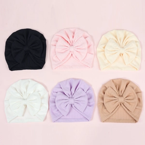 Flat lay of newborn turban hats with oversized bows in six solid colors and ribbed texture