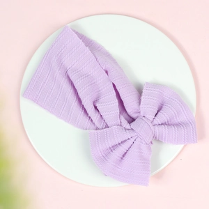 Close-up of a purple knitted baby headband featuring a large bow and ribbed texture