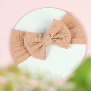 Elastic ribbed infant headband with a large layered bow in soft apricot pink color