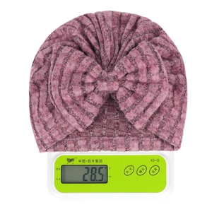 Détail d'un bonnet en tricot rose pour nouveau-né avec nœud, pesé sur une balance