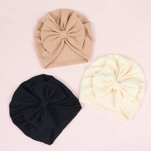 Detail of ribbed knit baby turban hats with large bow accents in khaki, cream, and black