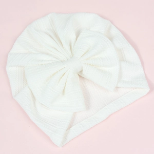 Detail of white waffle knit newborn turban hat with a large bow on pink background