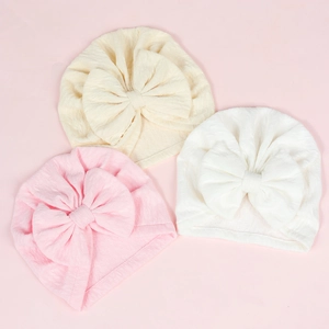 Detailed texture of baby beanies with oversized bows in cream, pink, and white colors