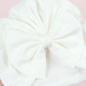 Detailed view of white baby turban with textured knit fabric and large decorative bow