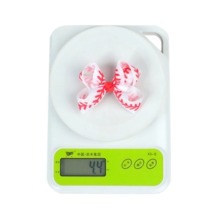 Macro detail of a 3-inch baseball print bow hair clip on a scale showing 4.4g weight