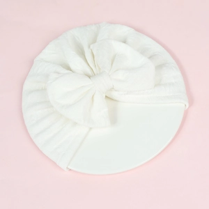 White newborn turban hat with large bow and knitted texture on a pink background