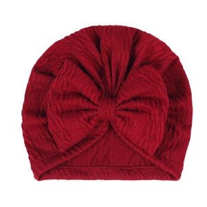 Detail of baby turban hat with large bow in dark red soft knitted fabric texture
