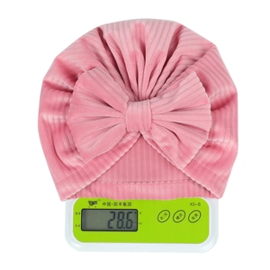 Pink newborn turban hat with bow knot showing lightweight weight on scales