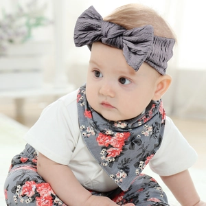 Détail d'un bandeau à nœud gris foncé et d'un bavoir floral assorti sur un bébé