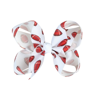 Close-up of white grosgrain ribbon hair bow with red football pattern and alligator clip