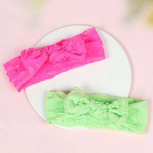 Detail of two elastic baby headbands in rose red and green with heart texture and bows